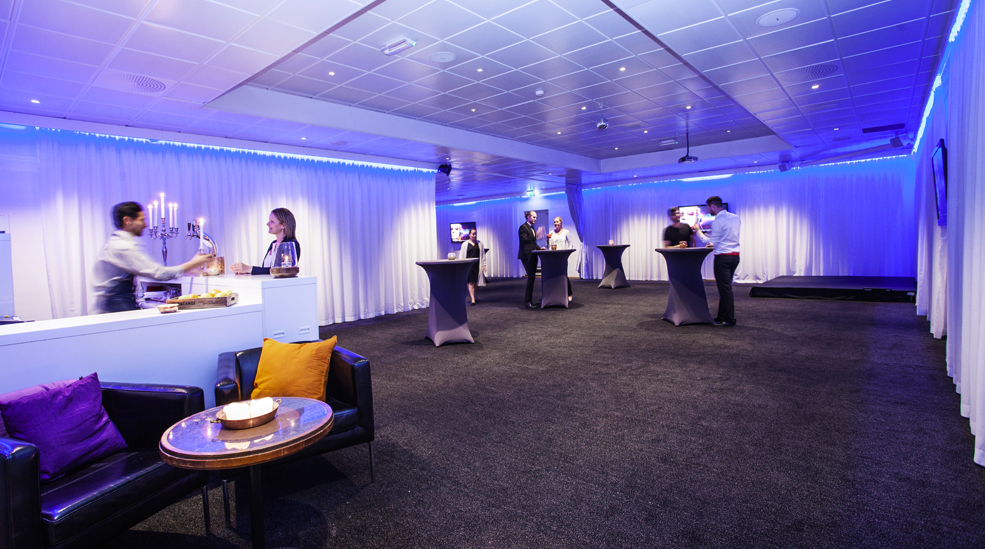 Cl_Gillet_Eventroom_mingel Modern kantig byggnad i glas och aluminium mot blå himmel. Foto.